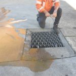 A man is engaging the DrainSAFE unit by turning the handle to isolate the storm drain from the spill that has occurred in a parking lot