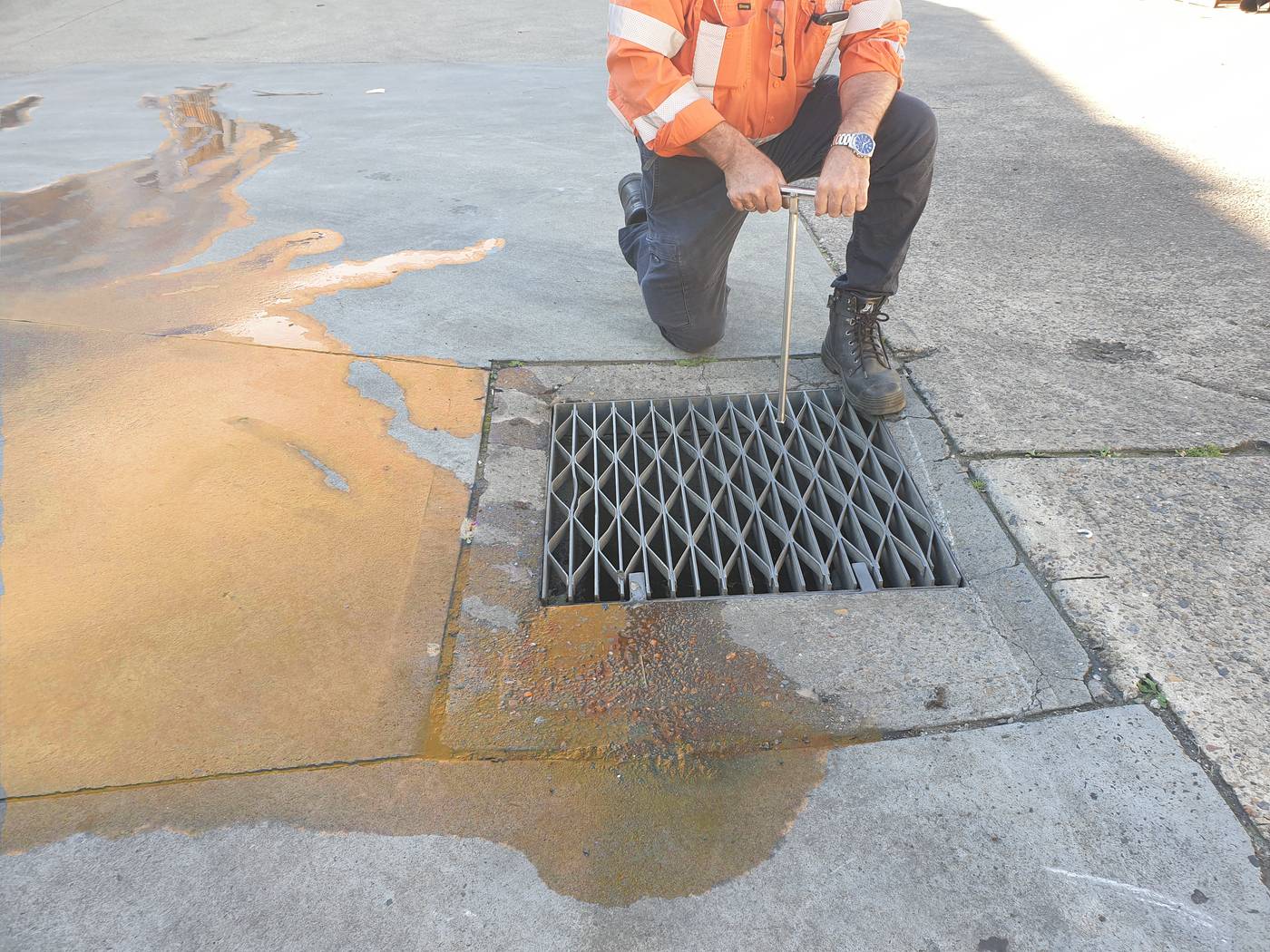 A man is engaging the DrainSAFE unit by turning the handle to isolate the storm drain from the spill that has occurred in a parking lot