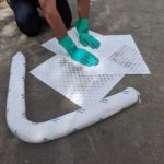 a person wearing gloves is absorbing a spill on the ground using pads and booms for spill clean up