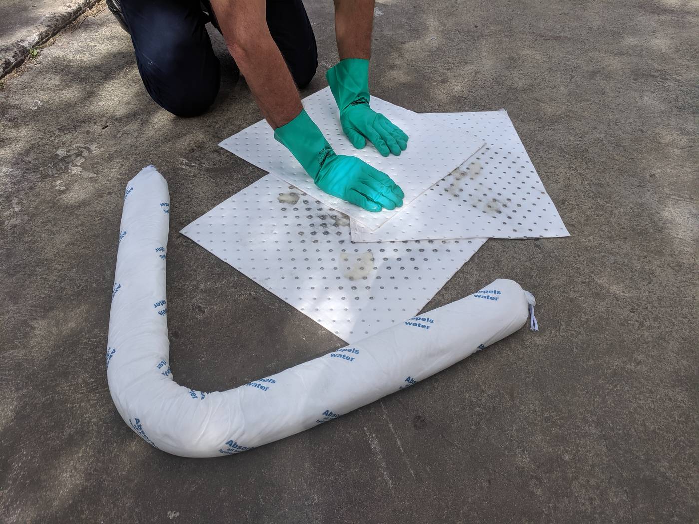 a person wearing gloves is absorbing a spill on the ground using pads and booms for spill clean up