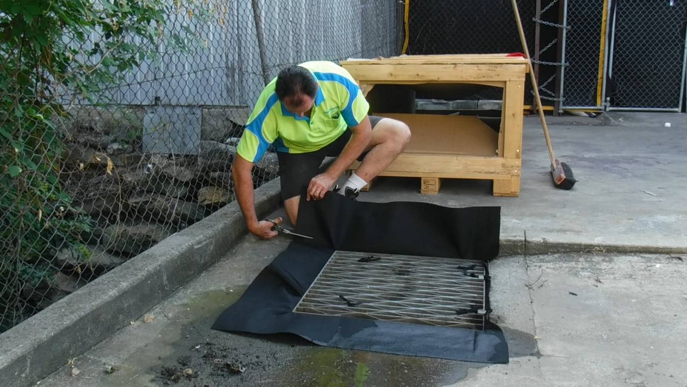 a man is trimming away the excess material from a drain warden installed in a drain pit